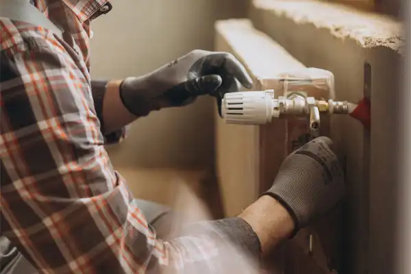 A person in a plaid shirt and gloves carefully adjusts a radiator valve indoors, demonstrating skills that extend to dehumidifier repair.