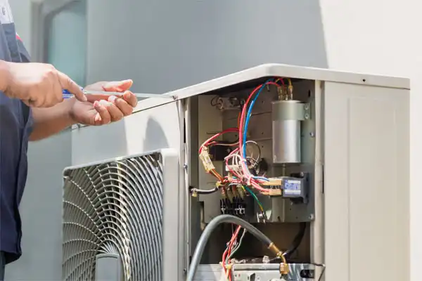 Person repairing an outdoor air conditioning unit, with the cover open to reveal wires and components.