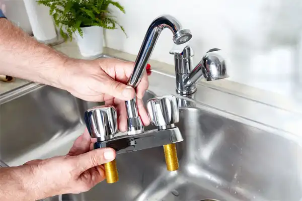 Hands holding a disassembled kitchen faucet over a sink, with a plant in the background.