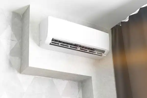 Wall-mounted air conditioning unit installed in a room, mounted near the ceiling, adjacent to a dark curtain.