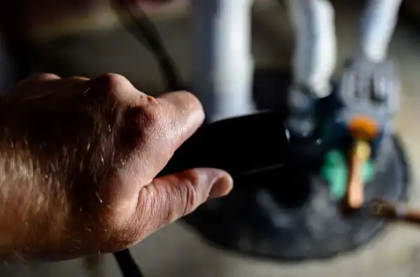 A hand is holding a black handle, with a blurred background showing part of a statue or figurine on a surface.