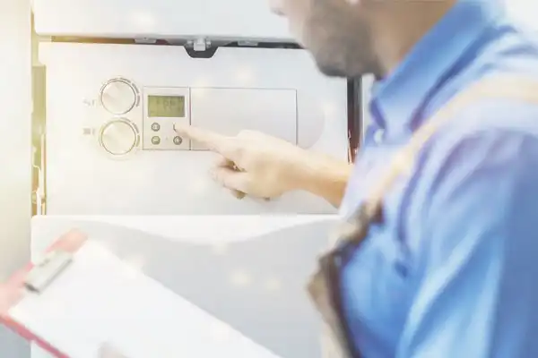 Person in blue shirt and suspenders adjusts controls on a wall-mounted device, holding a clipboard.