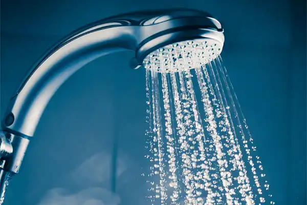 Close-up of a silver shower head with water streaming down, set against a blue background.