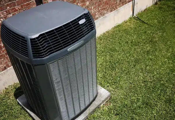 Outdoor air conditioning unit next to a red brick wall on a grassy lawn.