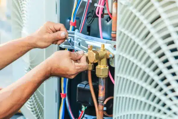 Hands working on an air conditioning unit, adjusting wires and components with a wrench.
