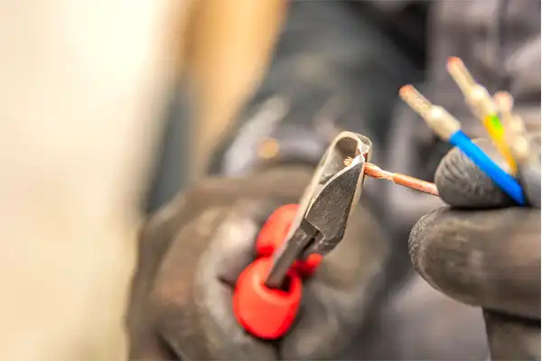 A person wearing gloves uses orange-handled wire cutters to cut electrical wires.