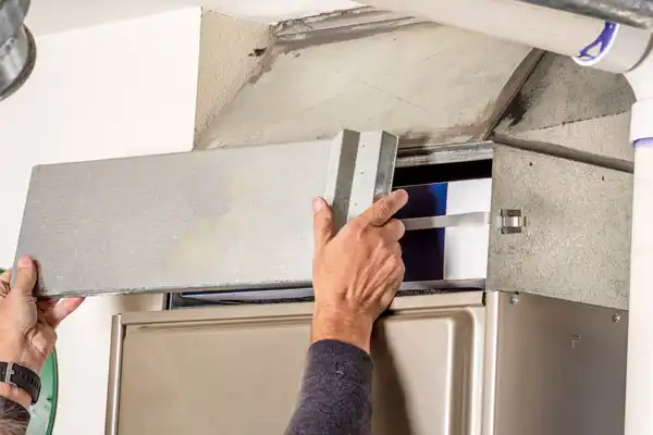 Person removing the cover from a home air filter compartment for maintenance.