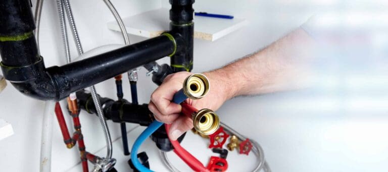 Person holding red and blue hoses near plumbing pipes and fittings in a utility area.