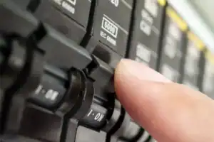 A close-up of a person’s finger flipping a switch on an electrical circuit breaker panel.