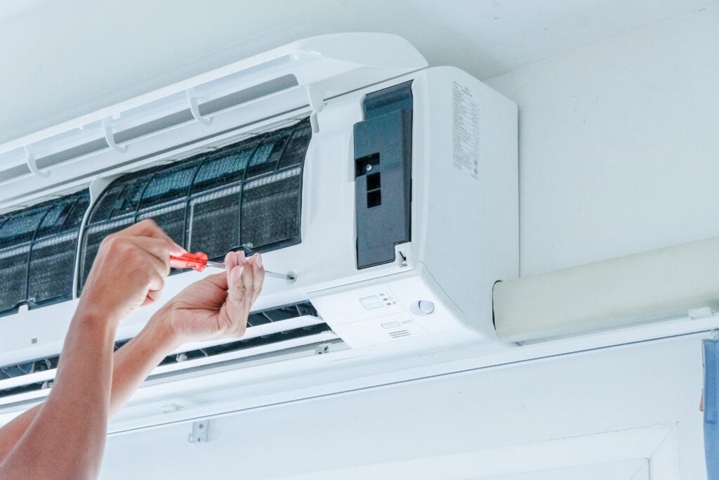 A person uses a screwdriver to repair or maintain a wall-mounted air conditioning unit.